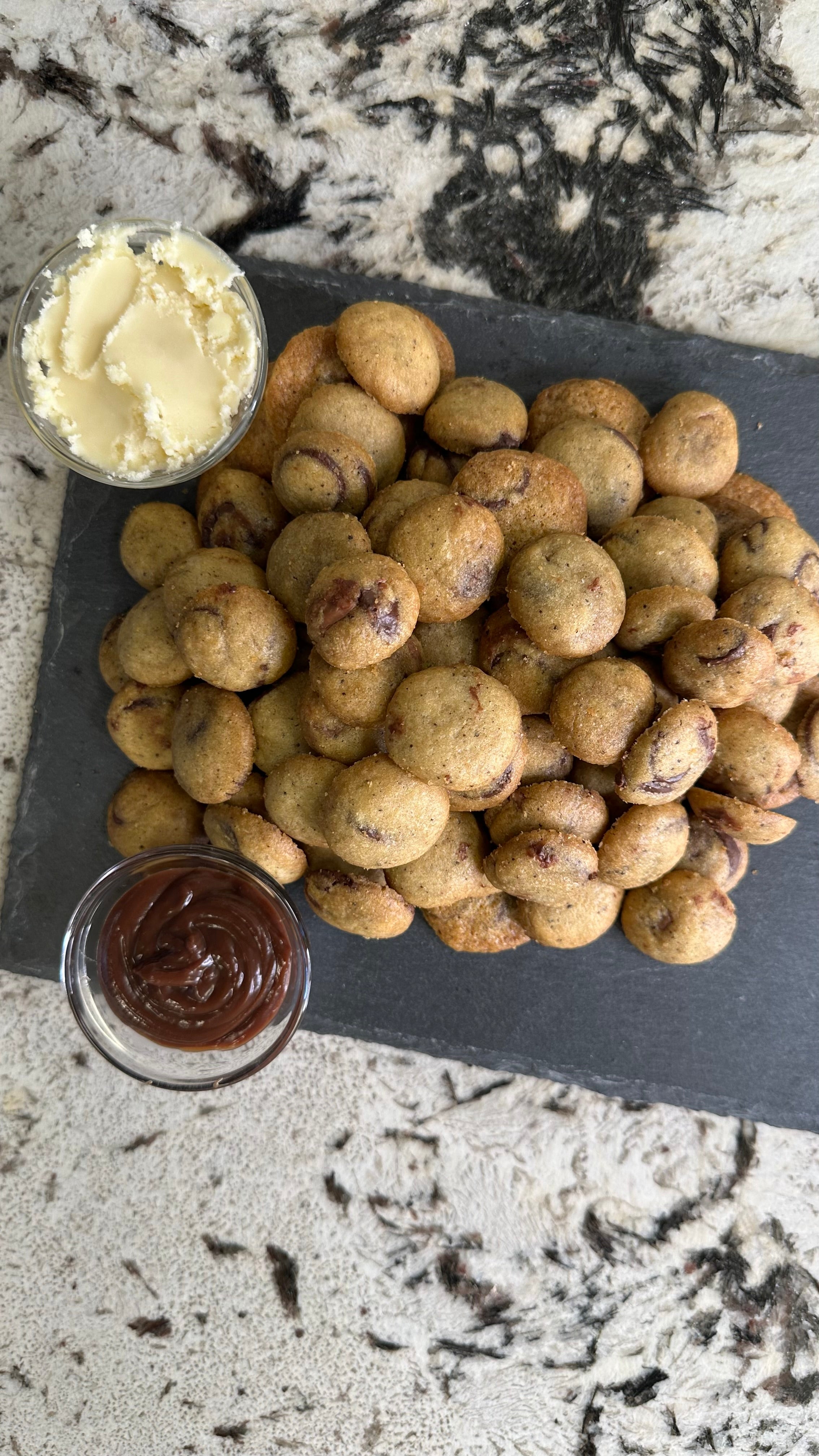 Cookie bites with a side of cheesecake ganache and chocolate ganache on a slate tray.